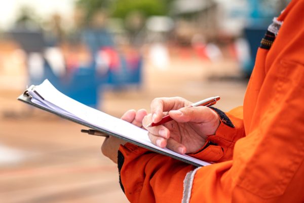 Action of safety officer is writing and check on checklist document during safety audit and inspection at drilling site operation. Industrial expertise occupation working scene.